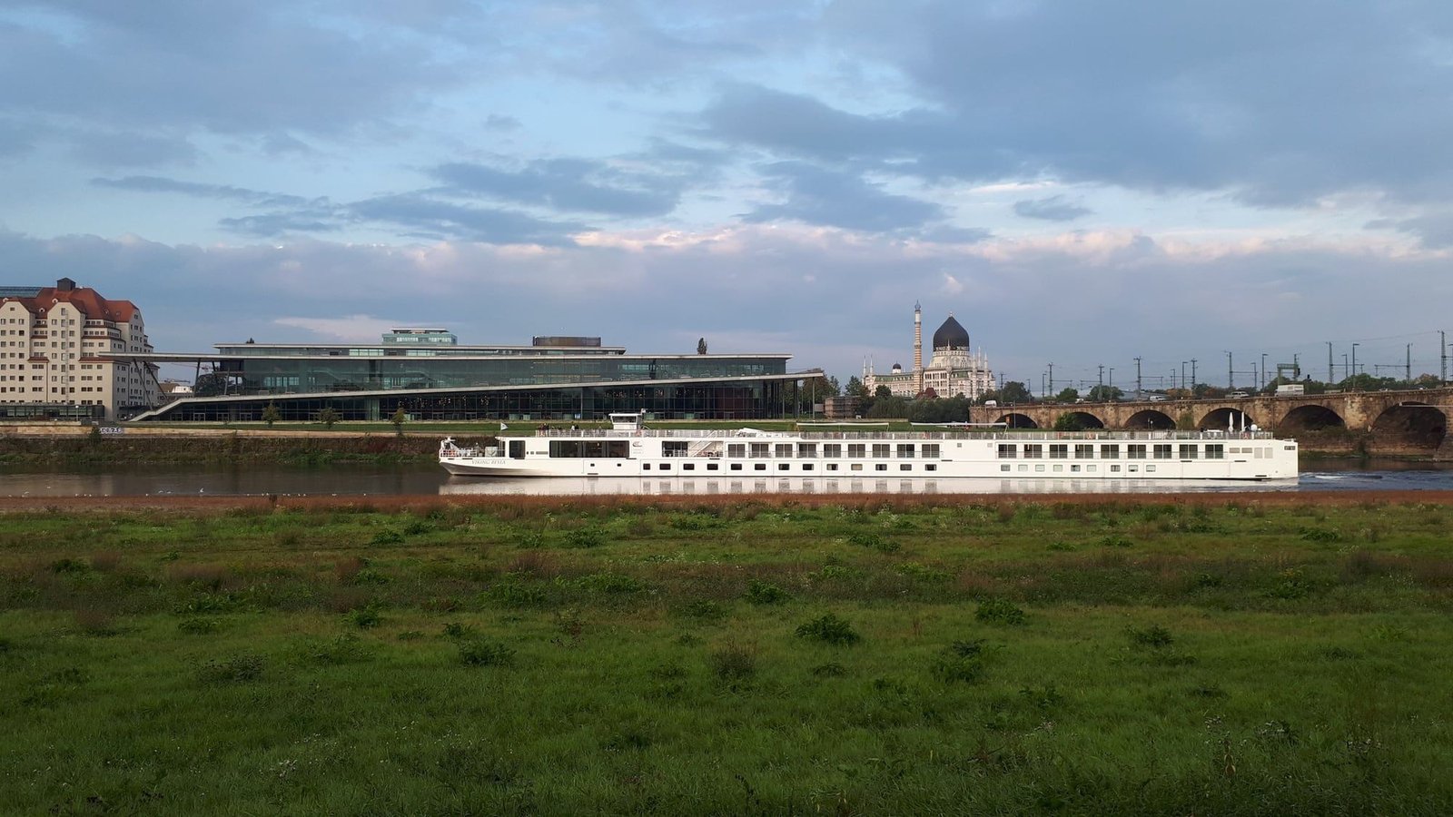 A river cruise ship gliding along the Elbe in Dresden, with the domed Yenidze and the Marienbrücke behind